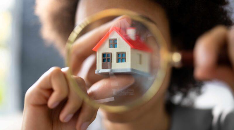 Detailaufnahme einer Person, die ein Miniaturhaus durch eine Lupe betrachtet, symbolisiert die sorgfältige Suche nach Immobilien mit einem Immobilienmakler in Düsseldorf